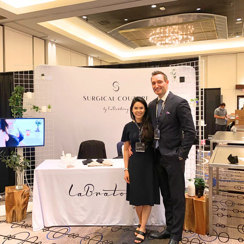 Two people standing in front of a 'Surgical Couture by LaBrato' booth at an event.