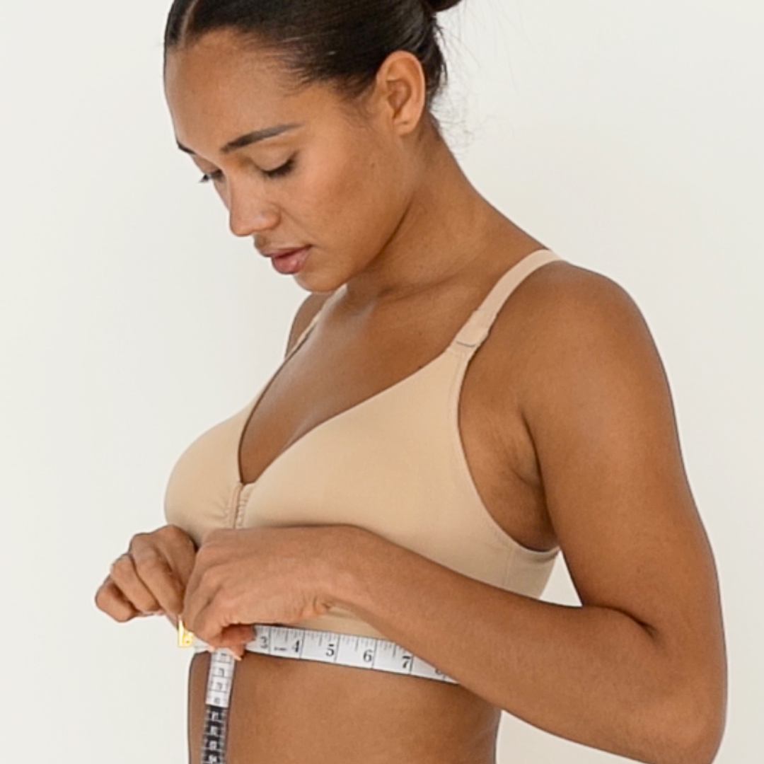 Woman measuring her bust with a tape measure against a plain background