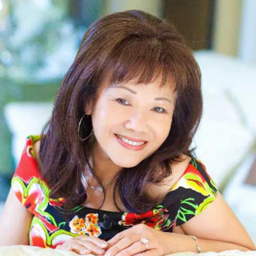Woman with short brown hair wearing a colorful floral top, sitting outdoors.