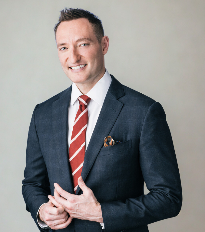 Man wearing a dark suit with a red striped tie against a plain background