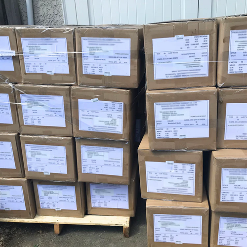 Stack of brown cardboard boxes with labels on a concrete floor.