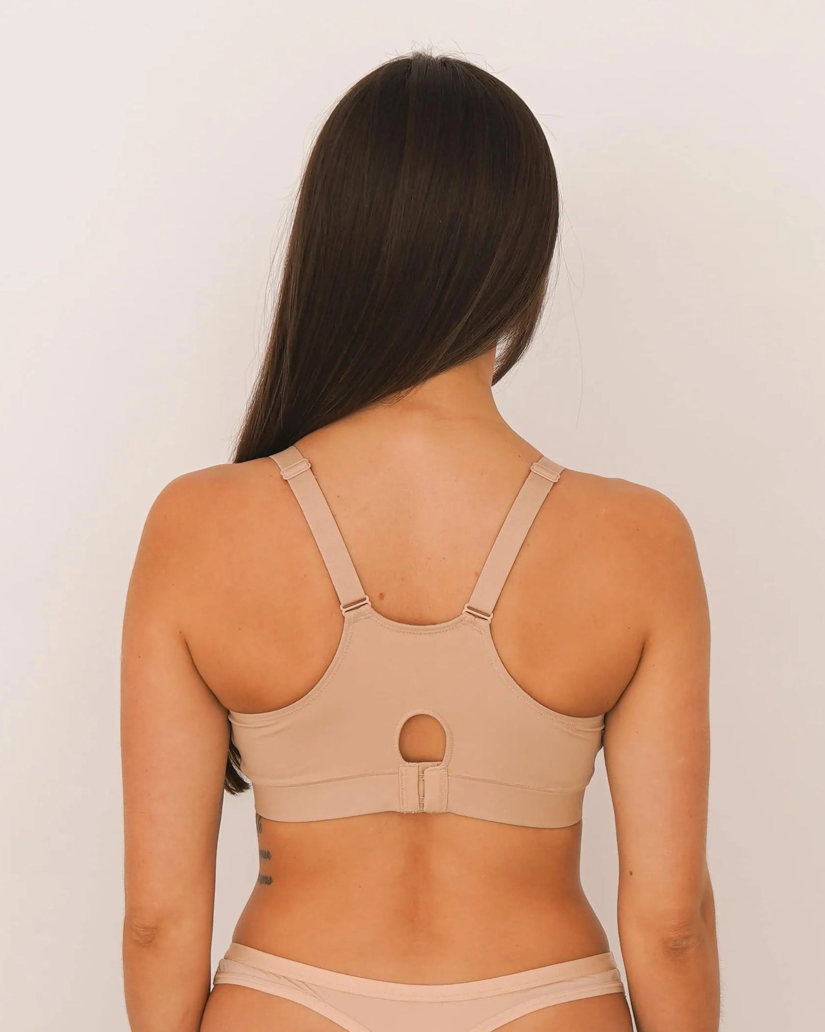 Woman wearing a beige bodysuit against a plain background