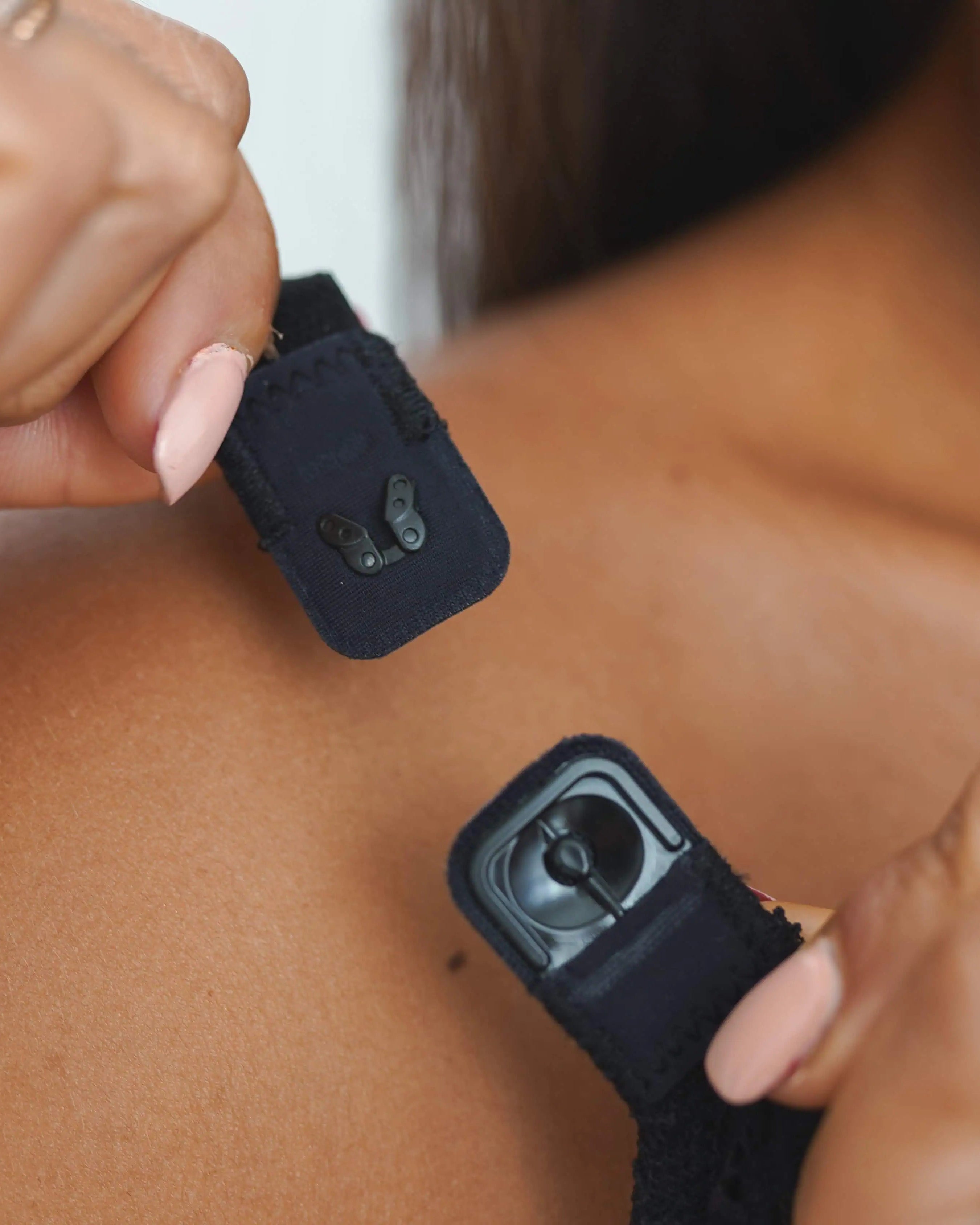 Person applying butterfly clasp on shoulder strap of compression surgical bra black