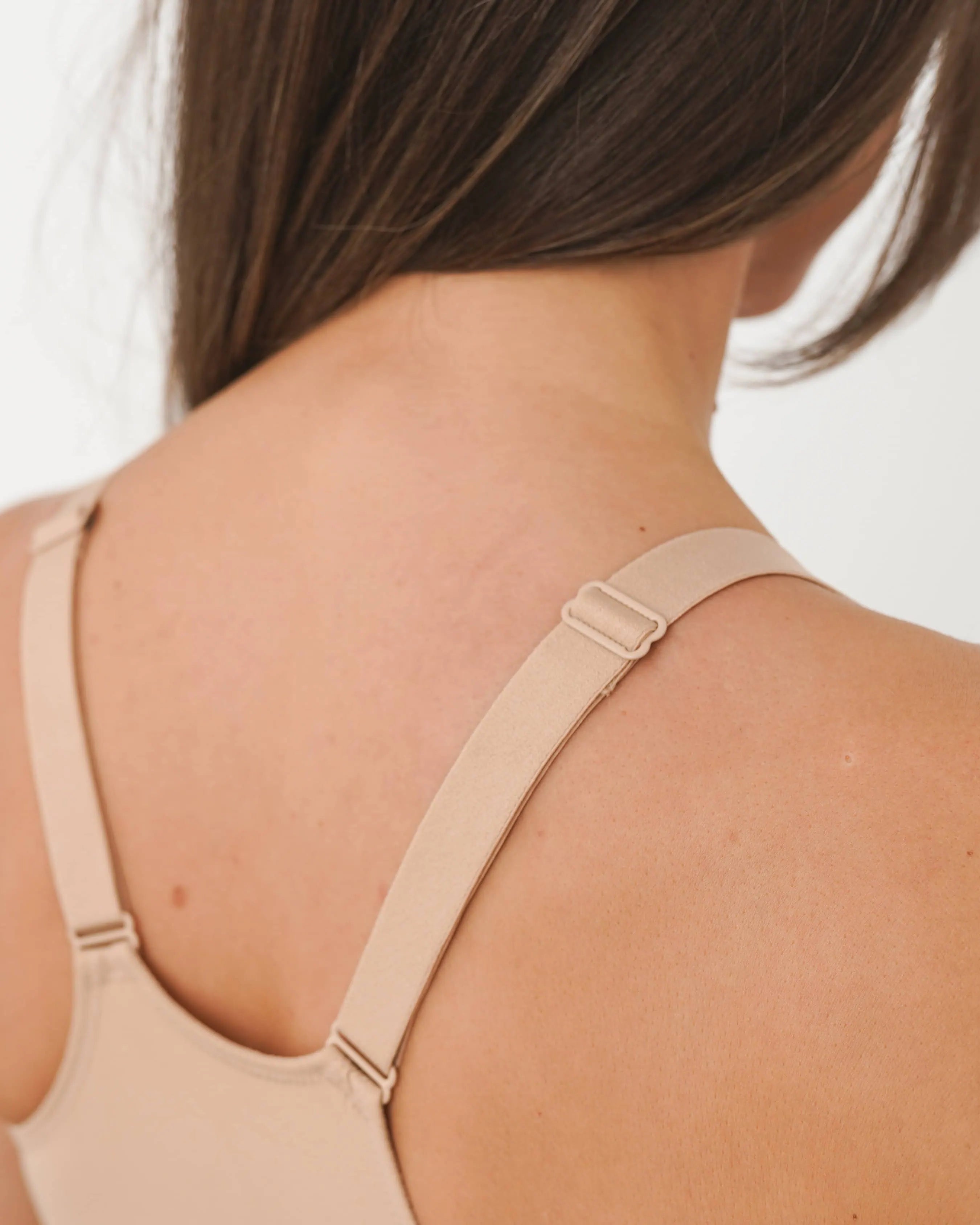 Person wearing a beige bralette against a neutral background